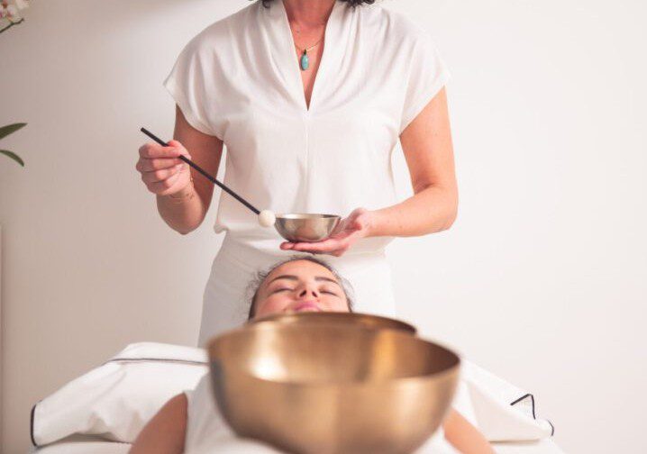 Woman receiving a relaxing facial treatment with a singing bowl nearby.
