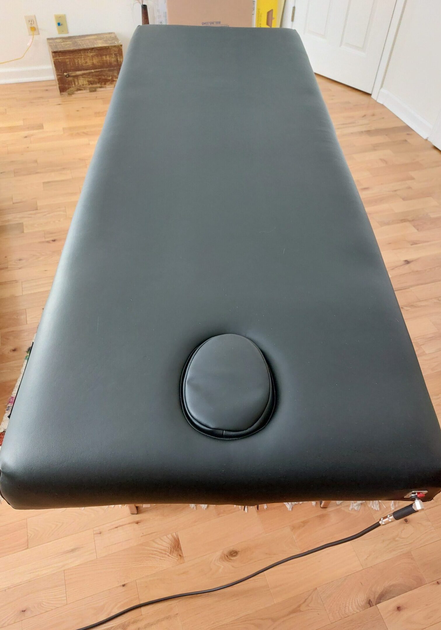 Black massage table with face cradle on wooden floor.